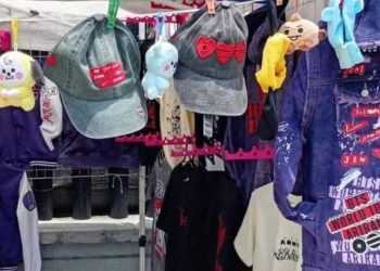 Clothes and accessories display: denim jackets, hats, and stuffed toys hanging on a market rack with pink clips and colorful decorations.