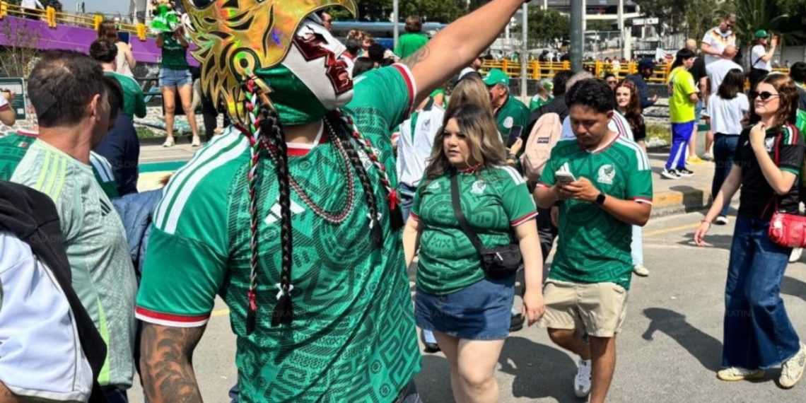 Crowd at an outdoor festival; a performer wearing a bright dragon mask and green patterned shirt leads a group in matching green jerseys.