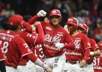 Red-uniform baseball players celebrate together on the field, with one central player raising a fist in triumph as teammates join in cheers.