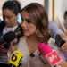 Woman being interviewed by several reporters with colorful microphones surrounding her outdoors.